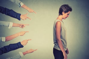 Concept of Industrial Revolution shame and accusation guilty school girl. Side profile sad upset girl looking down many fingers pointing at her back isolated on grey office wall background. Human face expression emotion sadness and FEAR