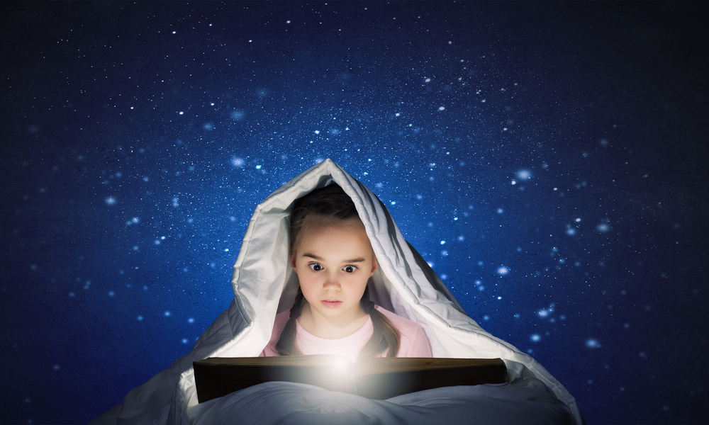 Cute scared girl in bed under blanket with book in hands, FEARfully reading.